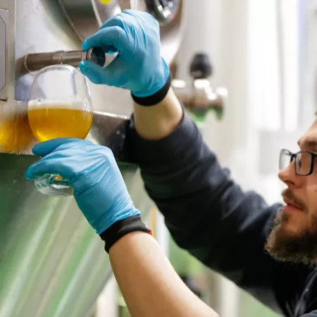 individual pouring beer from fermentaiton vat