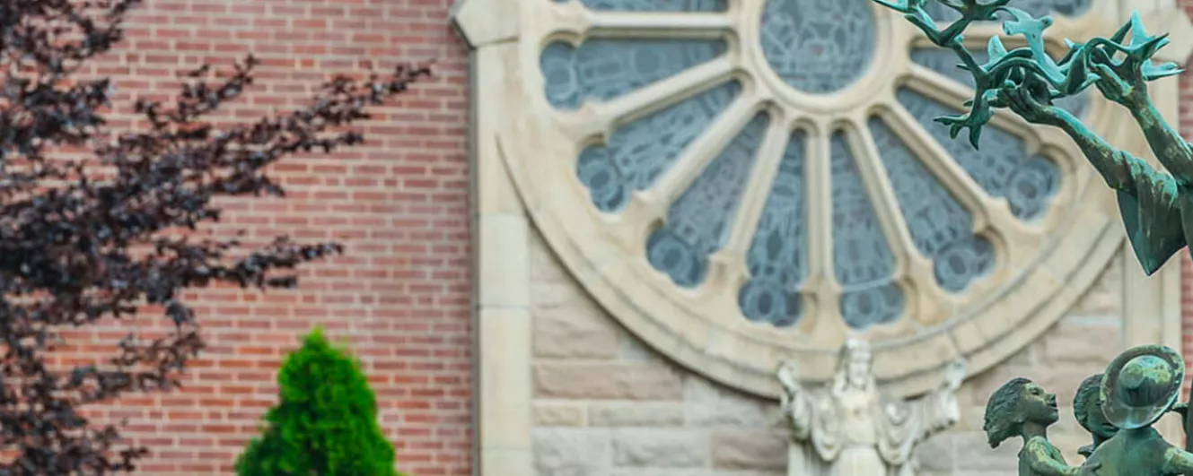 green statue of man holding birds or antlers. Children dance around him. Jesus is in the background.